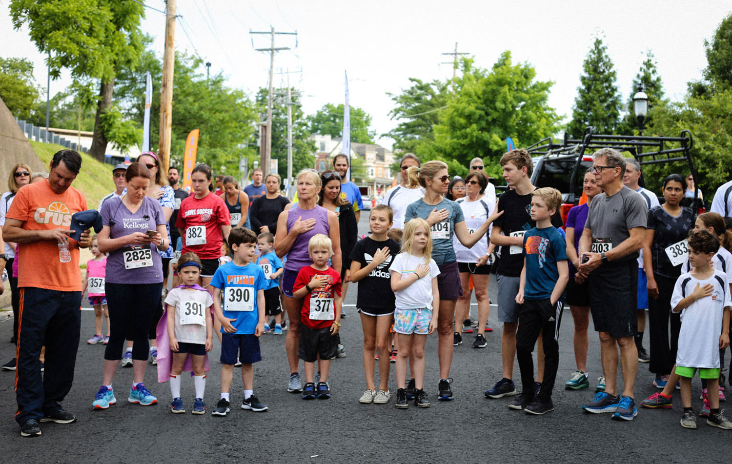 Runners and families standing with hands over their hearts for the national anthem at the start of the BCRR Twilight 5K